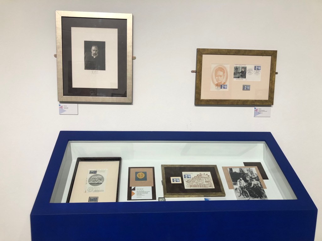 Display of documents and items related to Maria Sklodowska-Curie, including framed portraits and objects in a blue display case.