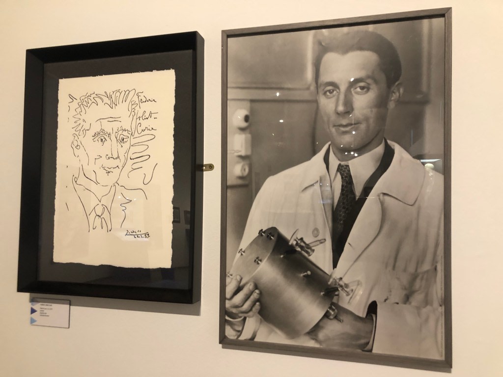 Line drawing of Pierre Curie on the left, with the artist's signature, and a black and white photograph of Pierre Curie holding laboratory equipment on the right.