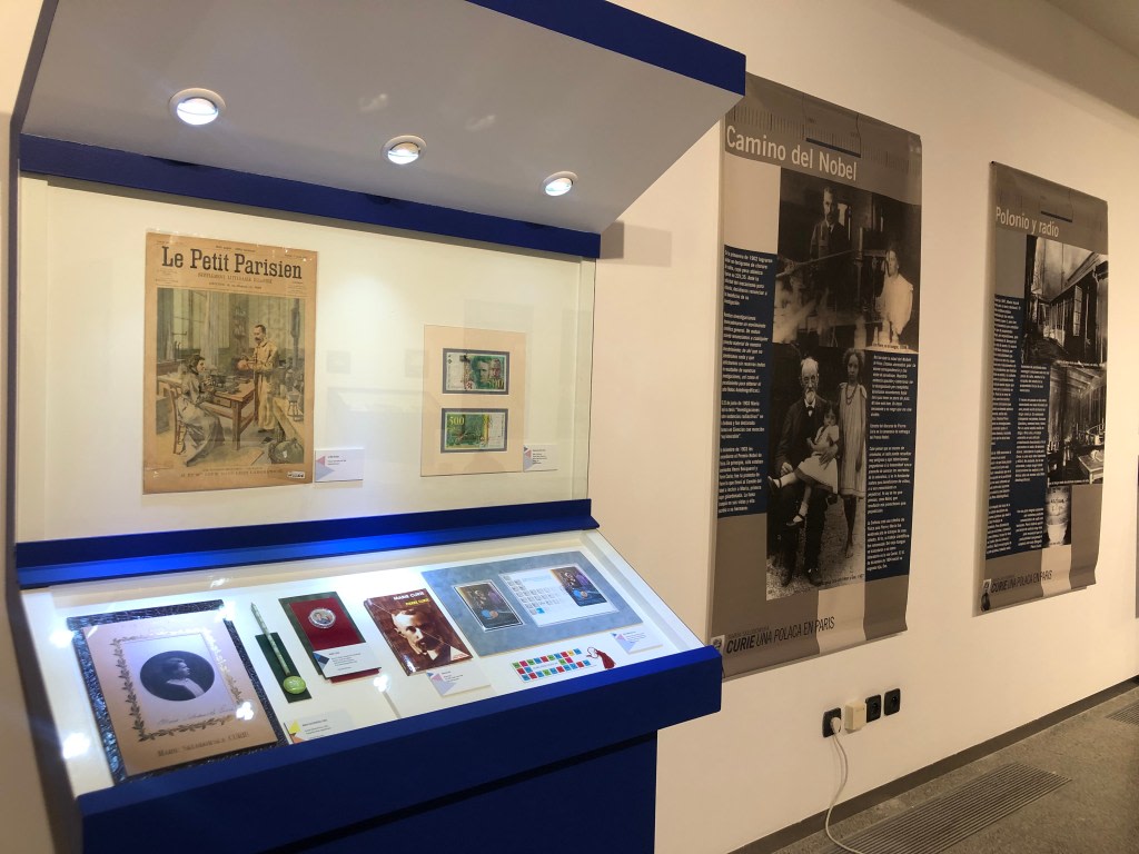 Display of objects and informational panels about the life and work of Marie Sklodowska-Curie, including articles from the journal