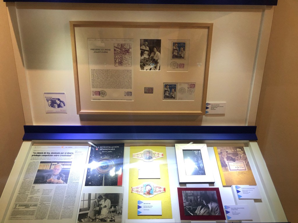 Display of documents and artifacts related to Irene Joliot-Curie and Frederic Joliot-Curie in a display case at the Maria Sklodowska-Curie exhibition.