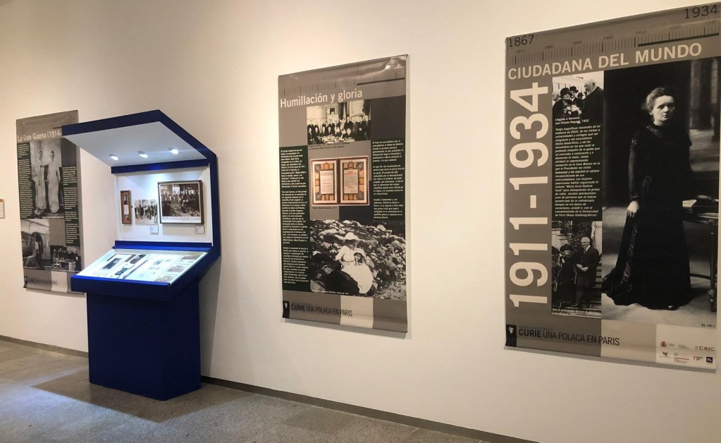 Exhibition about the life and work of Marie Sklodowska-Curie, including informational panels and display cases with objects and photographs, in an artistic space.