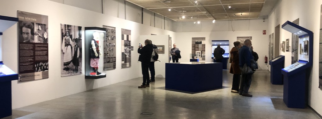 Exhibition about Maria Sklodowska-Curie, showing informational panels and display cases with related objects. Visitors observe the exhibit in a cultural setting.