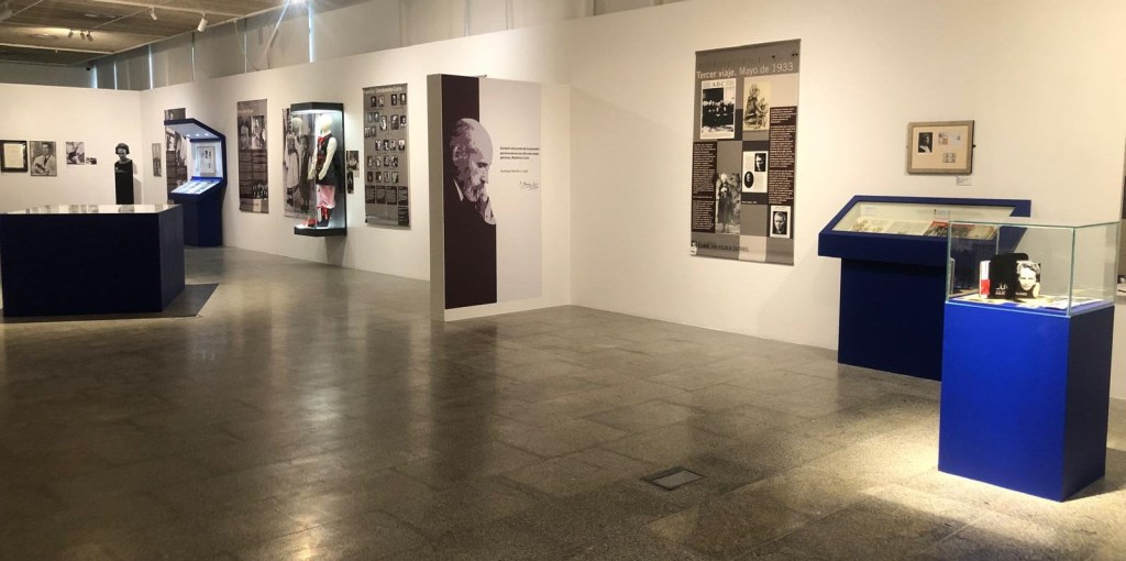 Interior view of the exhibition about Maria Sklodowska-Curie, showing informational panels, display cases with related objects, and photographs on the walls.