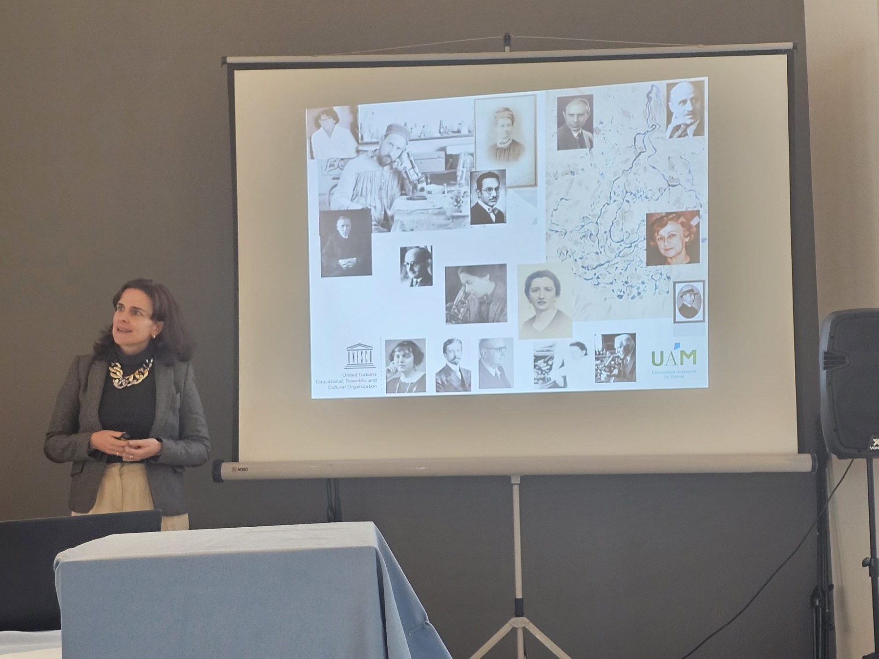 Presenter at an event about Santiago Ramón y Cajal, alongside a projection of historical images of scientists related to neuroscience.