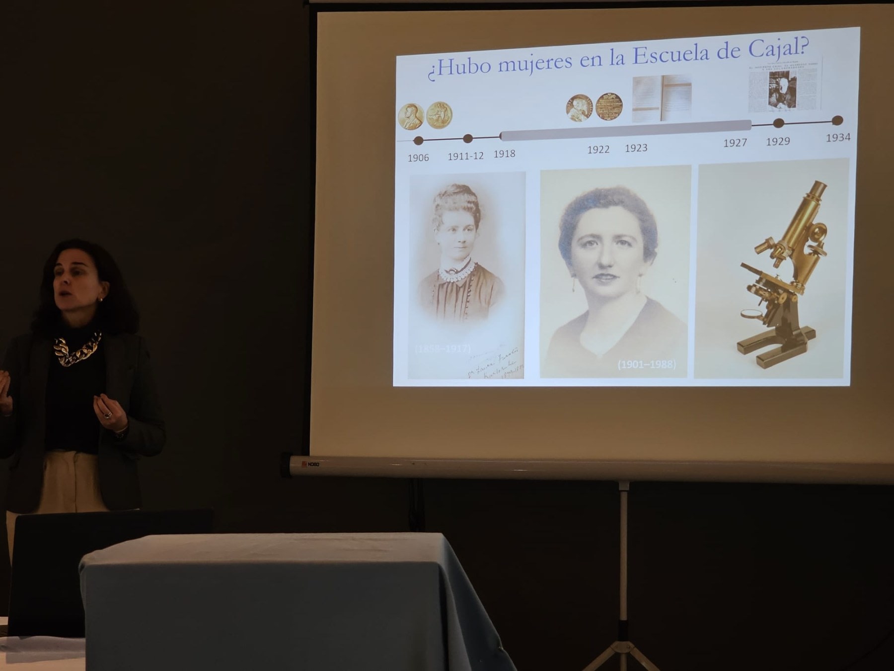A presenter speaks about women in Cajal's School, alongside a presentation featuring photos of women scientists and a microscope.