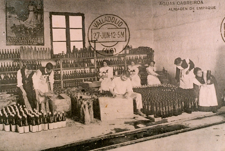 Interior de un almacén de empaque de Aguas Cabreiroá, con varios trabajadores organizando botellas en estantes y preparando el embotellado.