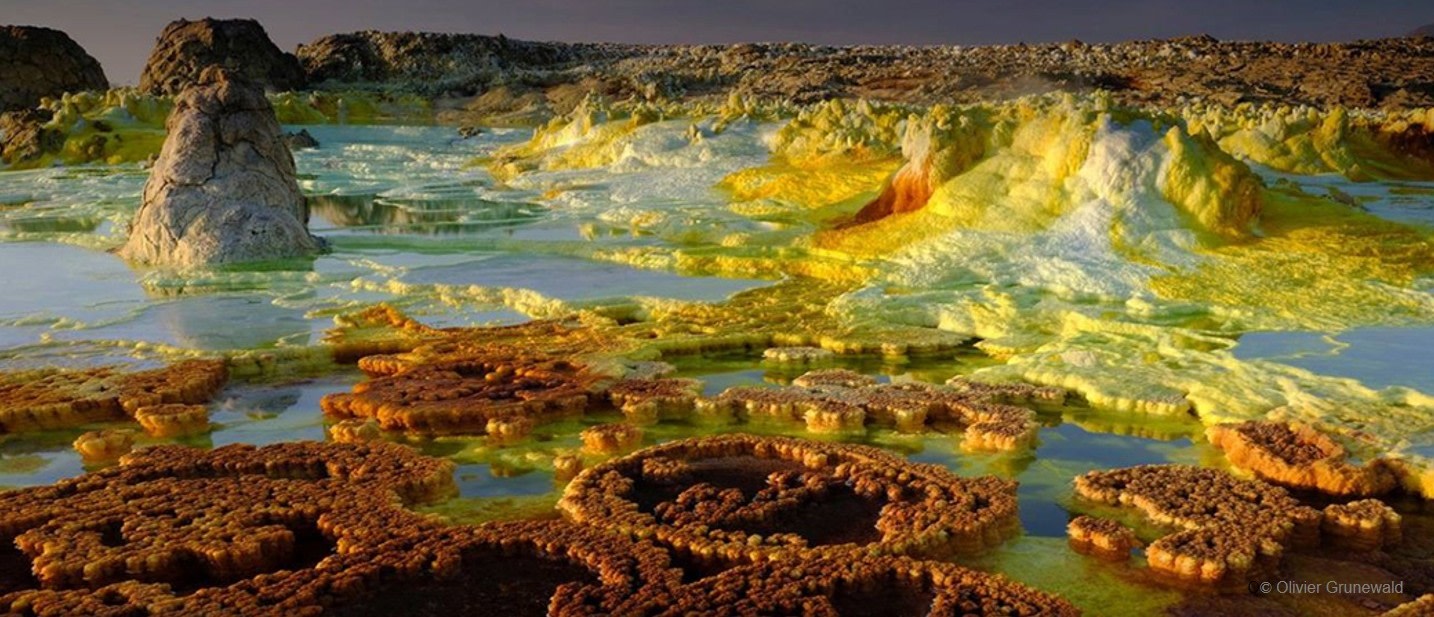 Paisaje natural de formaciones geológicas coloridas en un ambiente mineral con agua y tramos de terreno irregular.