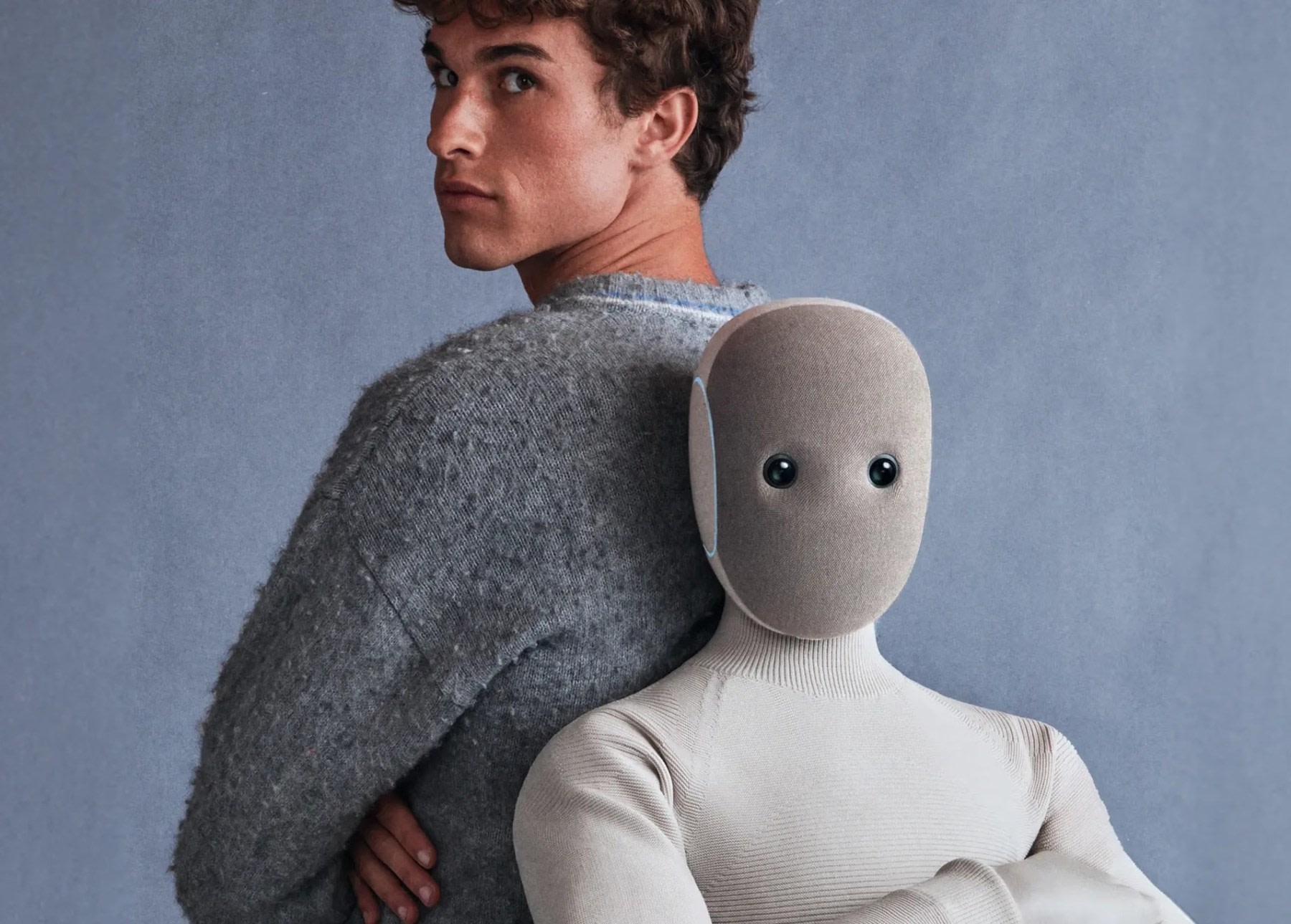 A male model posing from behind with a soft-textured humanoid figure, both in front of a grey background.