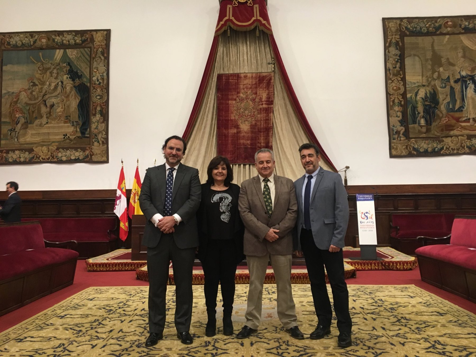 Ceremony in a hall decorated with University of Salamanca motifs, where several people stand before a podium, celebrating an event related to the Spanish School of Neurohistology.