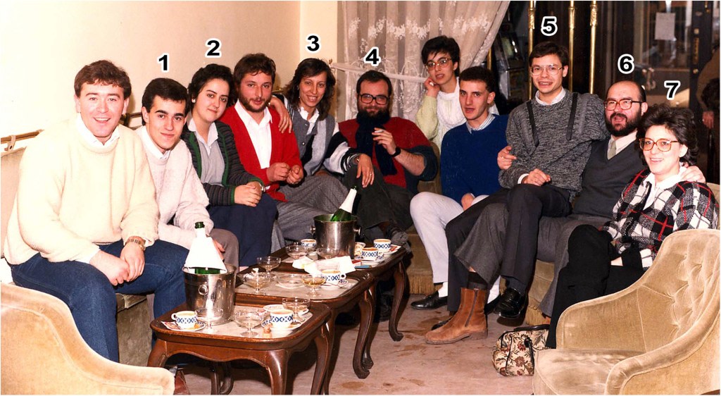 Group of people seated on a sofa with drinks at a social gathering, all smiling and conversing in a cozy atmosphere.