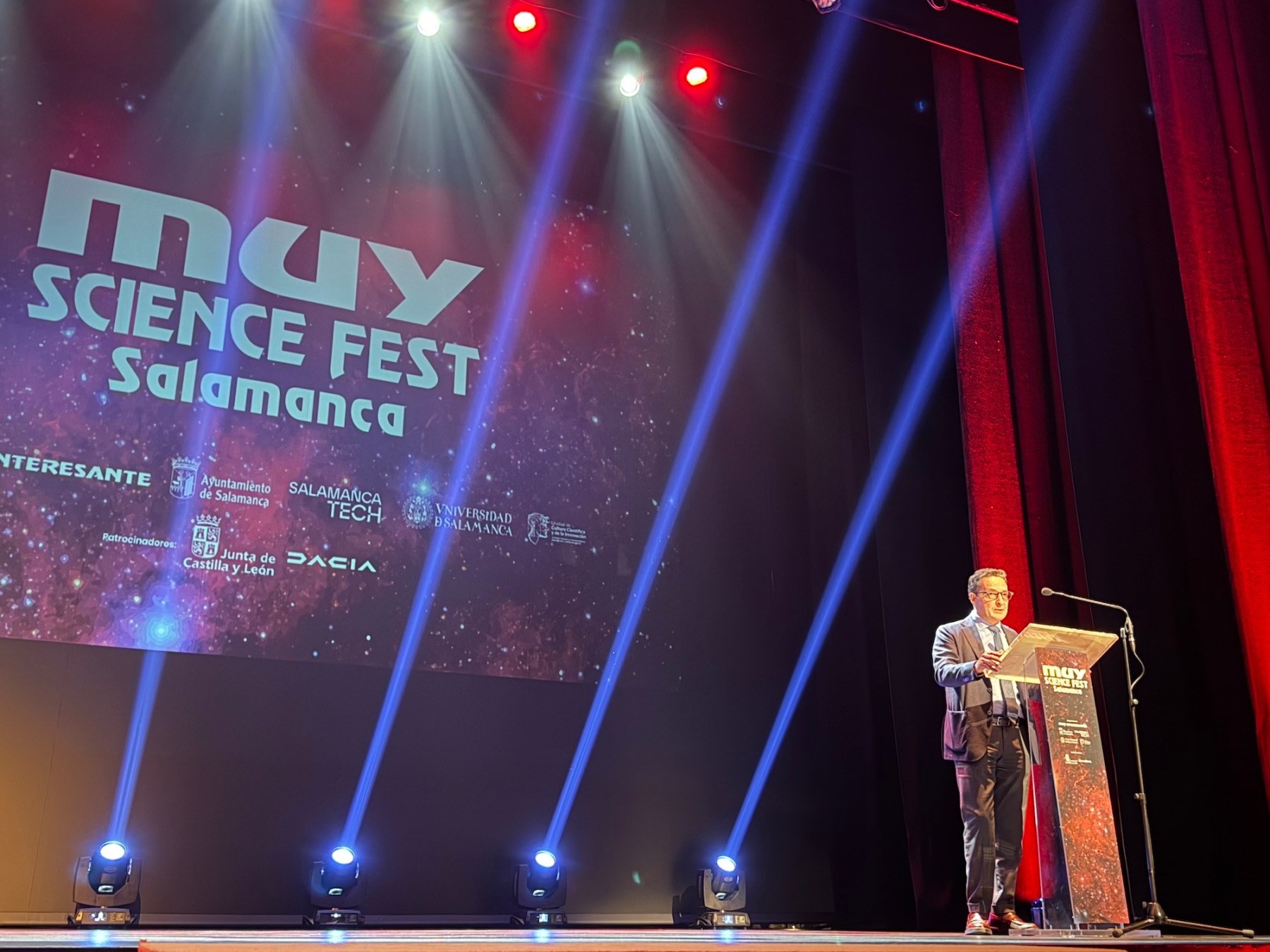 Un ponente en el escenario del MUY Science Fest 2025 en Salamanca, con un fondo iluminado que muestra el logotipo del festival y colores vibrantes.