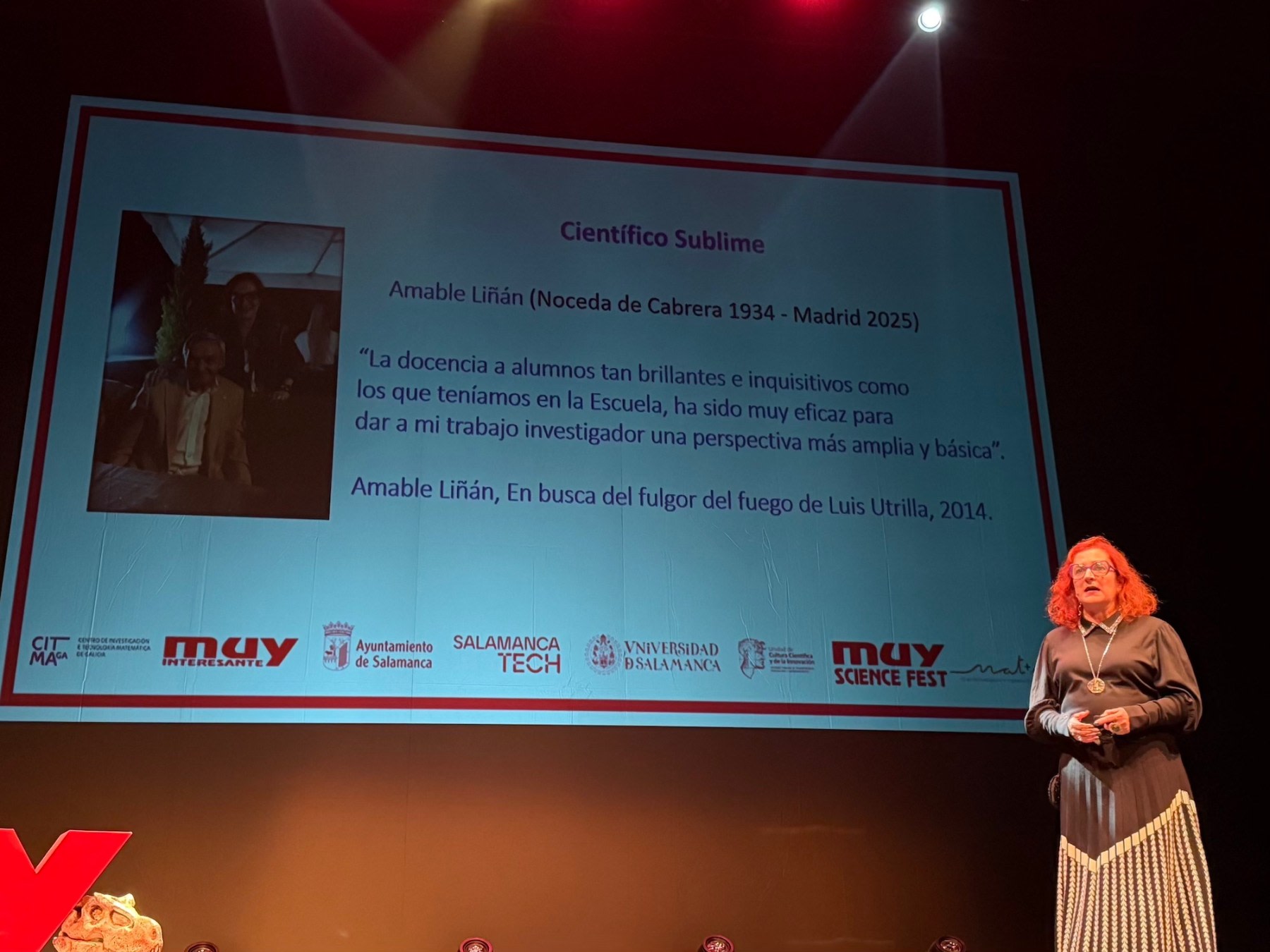 Una presentadora habla en el escenario del Teatro Liceo durante el MUY Science Fest 2025, con una proyección a su lado que muestra información sobre el científico Amable Liñán.