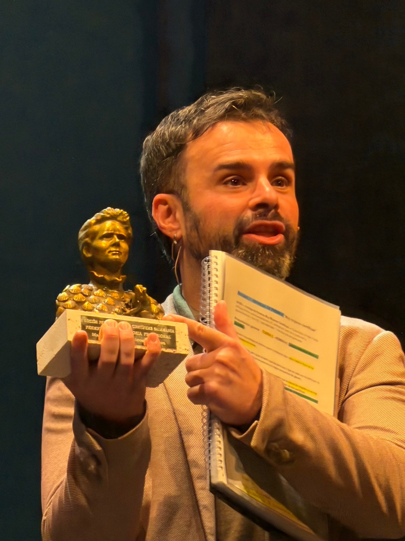 Presentador sosteniendo un trofeo dorado en un evento de ciencia, mostrando entusiasmo y dirección hacia la audiencia.