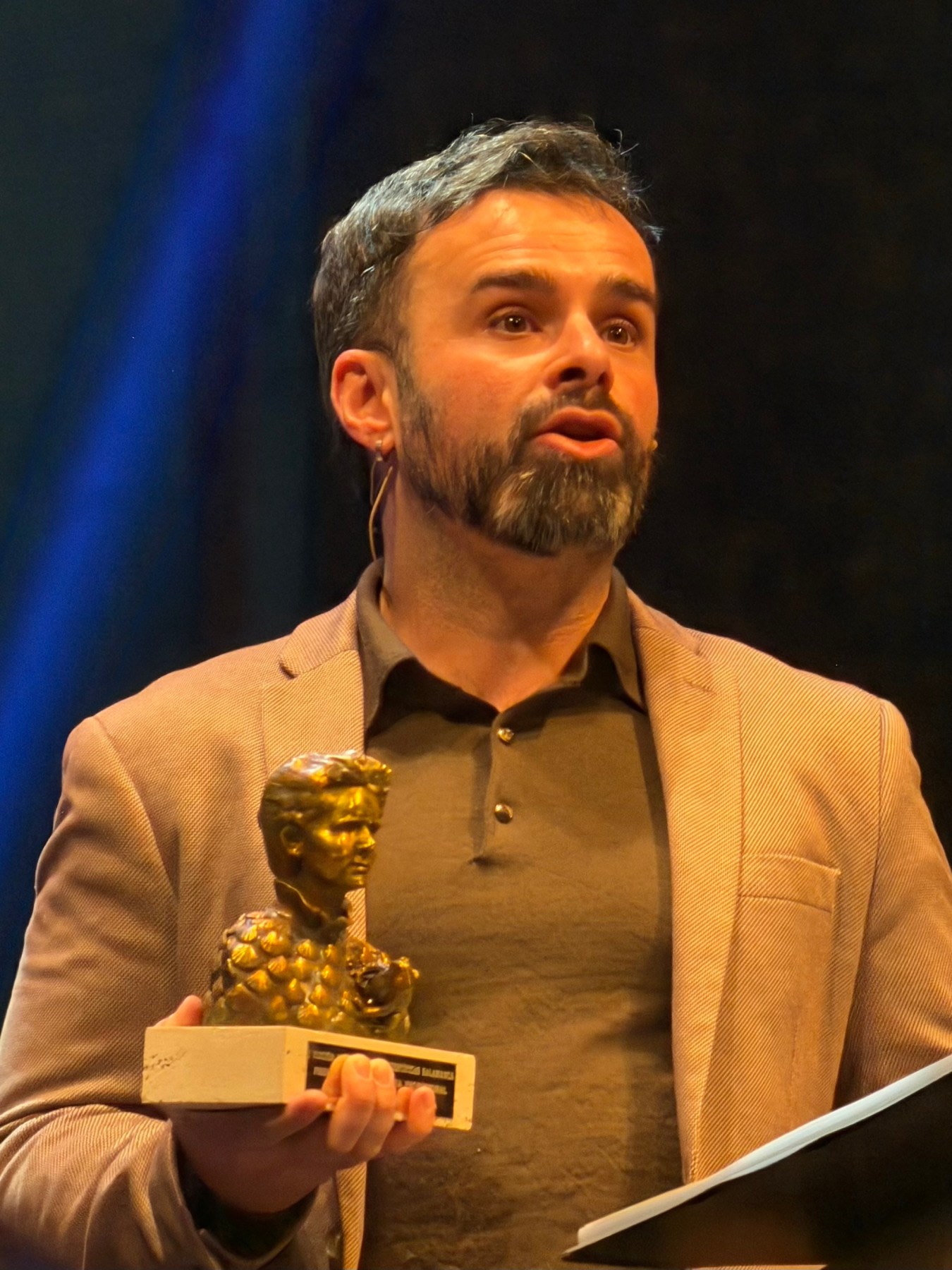 Hombre presentando un premio en un evento de ciencia, sosteniendo una estatuilla dorada en su mano mientras habla al público.