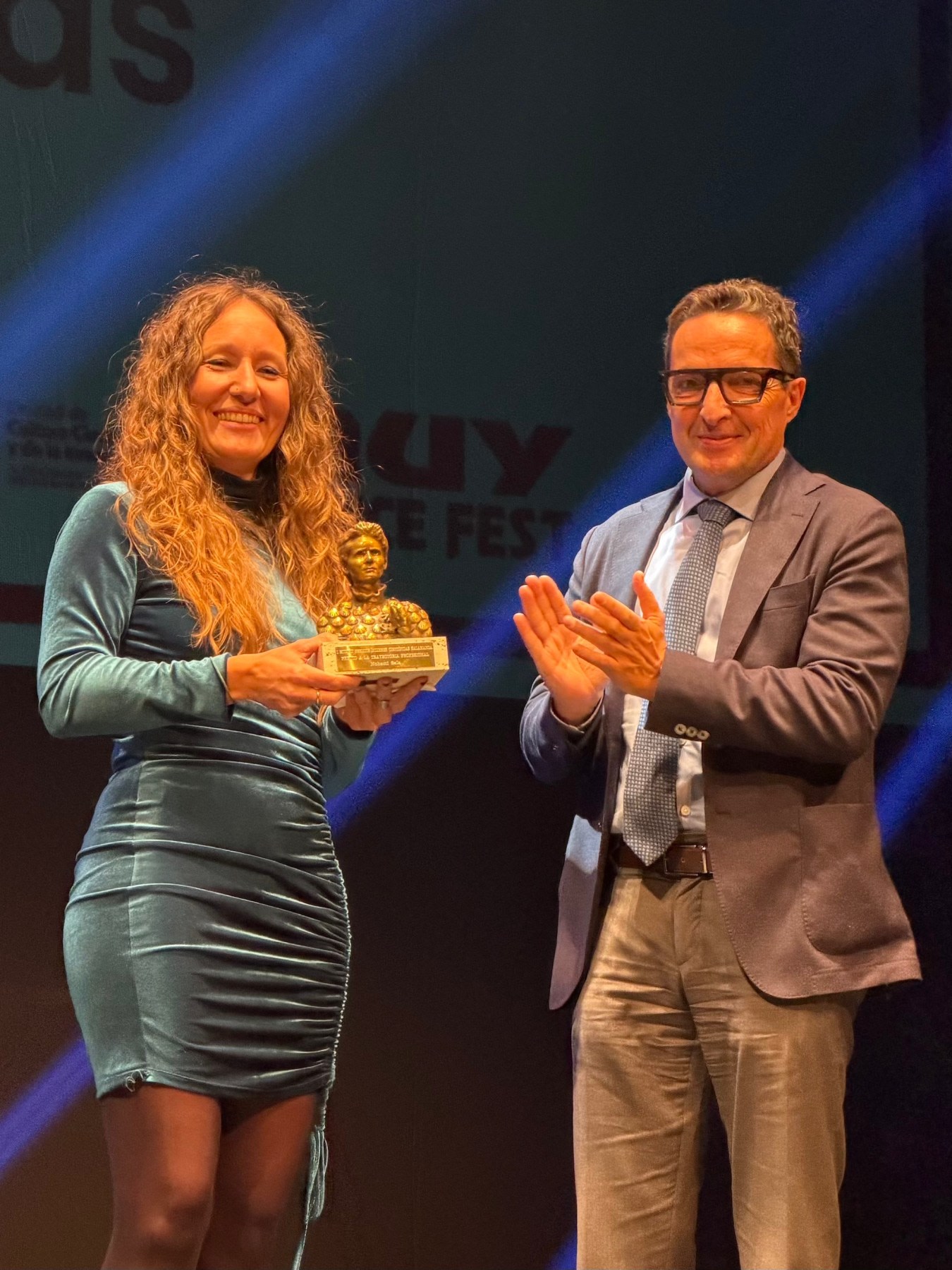 Entrega de premio en el MUY Science Fest 2025, con una mujer sosteniendo un trofeo mientras un hombre aplaude, en un escenario iluminado.