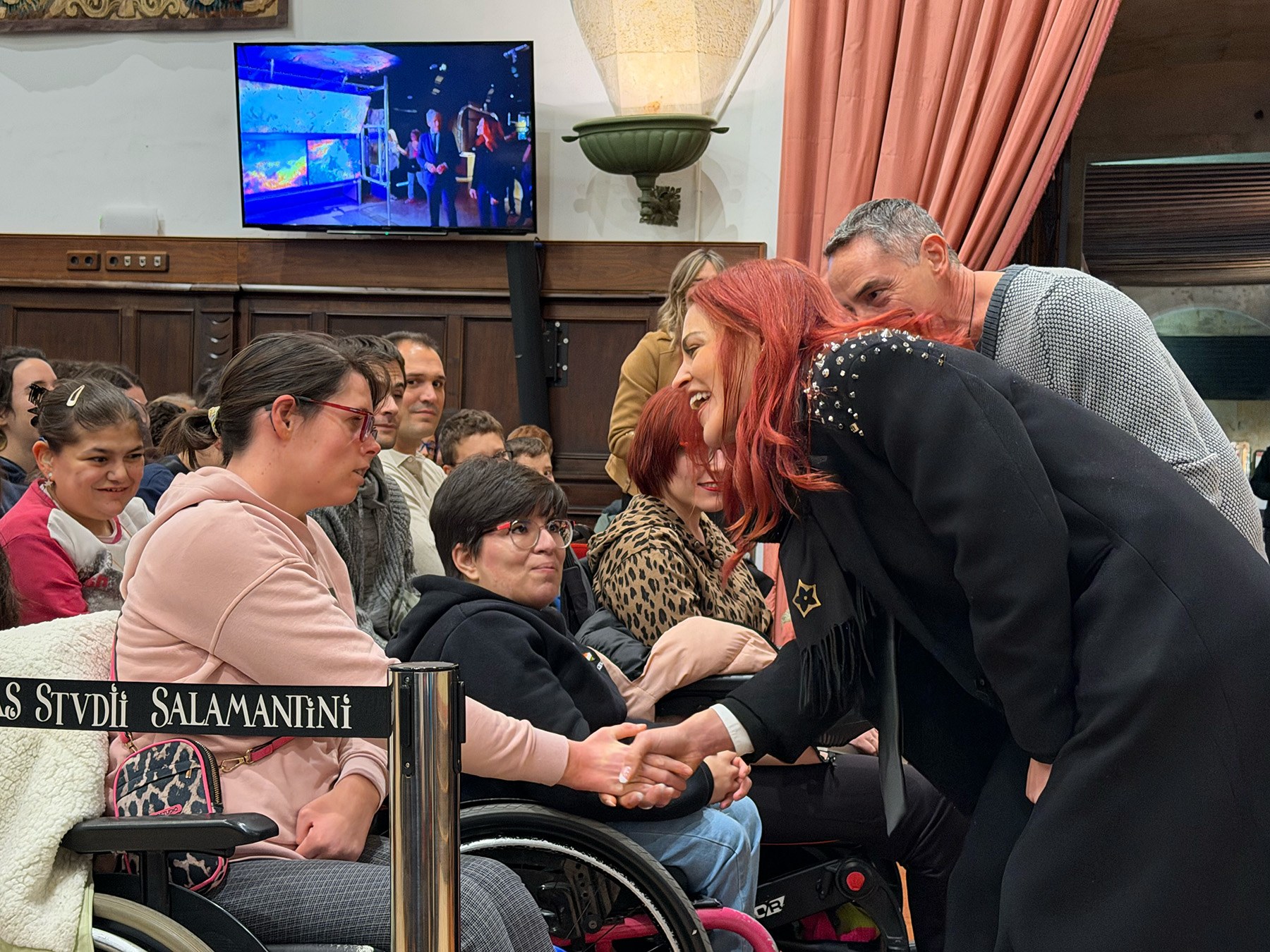 Sara García Alonso interactuando con un grupo de personas en un evento, mientras una pantalla al fondo muestra contenido relacionado con ciencia y exploración espacial.