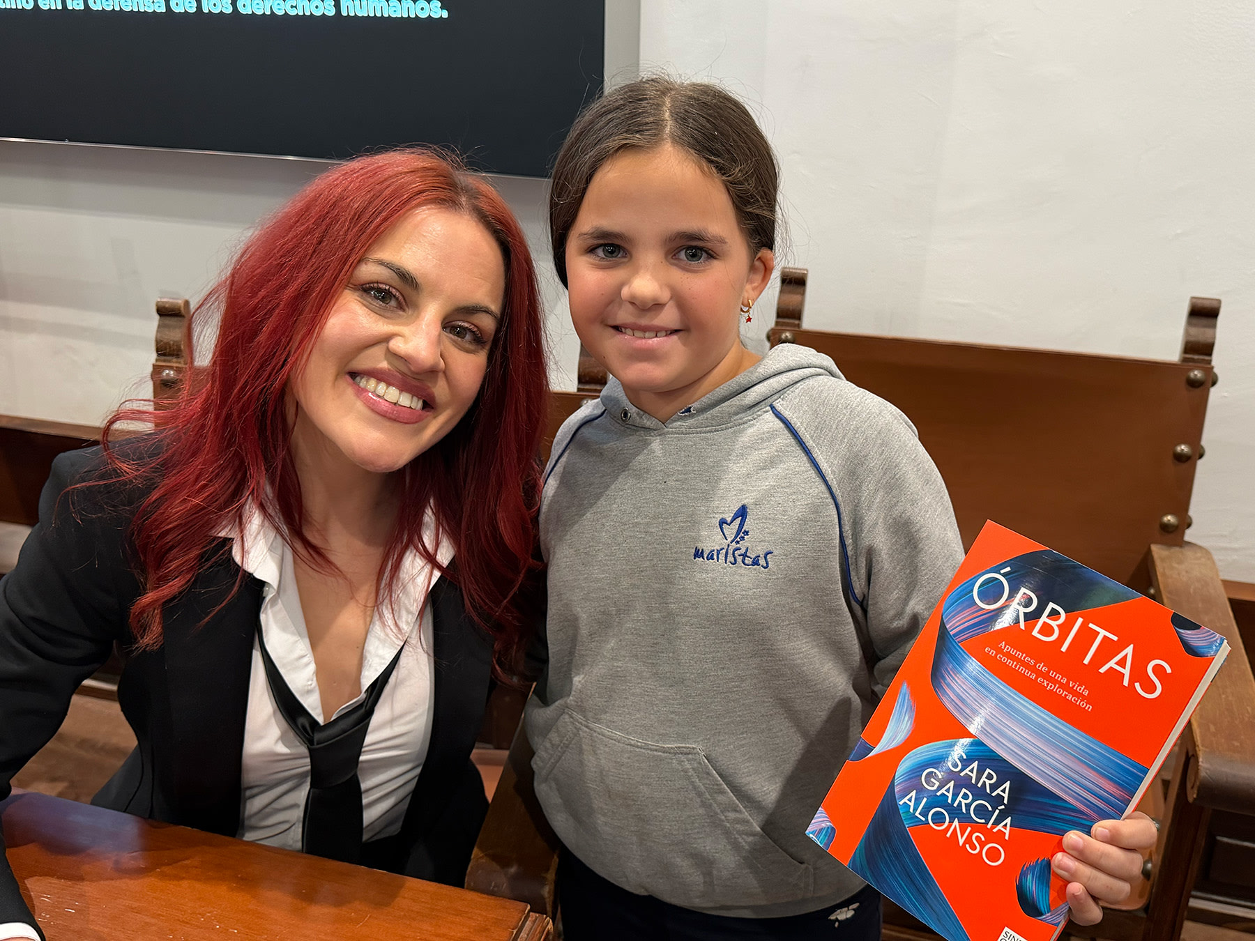 Sara García Alonso sonríe mientras posa junto a una niña que sostiene su libro 
