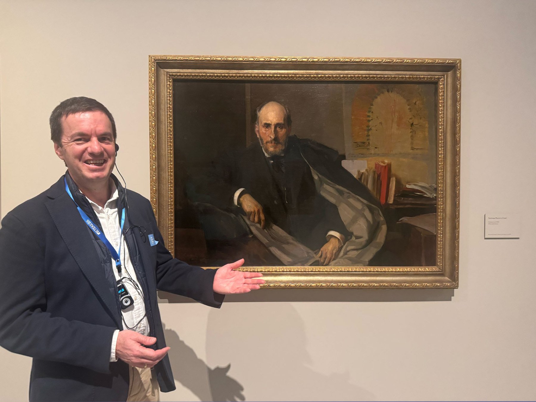 A smiling visitor points at a portrait in an art gallery, while the background features simple decorative elements.